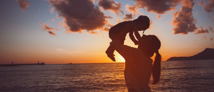 Silhueta de mãe segurando criança de colo acima da altura da cabeça