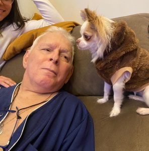 Um idoso em um sofá olhando para cachorro que está ao lado dele